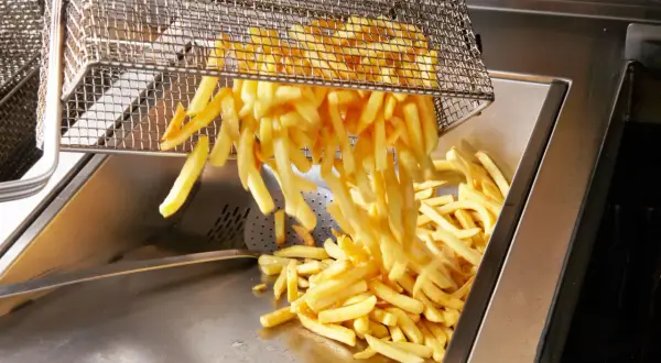 Frytki wysypywane z kosza do frytownicy. Nadmiar cukru w ziemniaku może powodować ciemnienie frytek podczas smażenia.