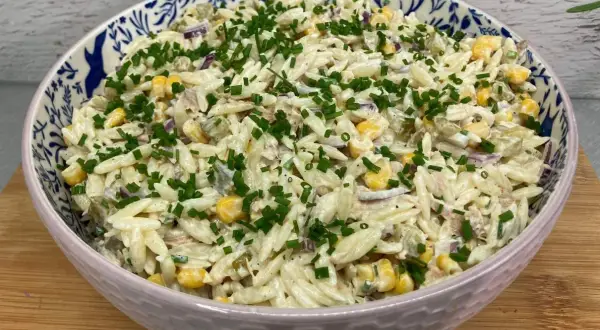 Pyszna sałatka z tuńczykiem i makaronem orzo, z kukurydzą i szczypiorkiem, w ozdobnej misce.