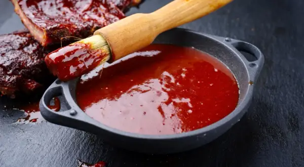 Pędzel zanurzony w sosie barbecue, gotowy do posmarowania żeber. Idealny przepis na to, jak zrobić sos barbecue.