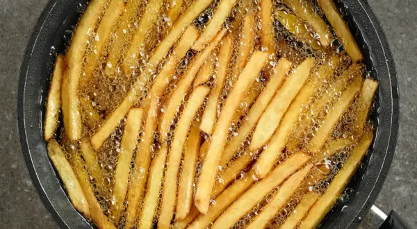 Smażone frytki w gorącym oleju. Aby uniknąć nasiąkania frytek tłuszczem, kluczowe jest utrzymanie wysokiej temperatury oleju.