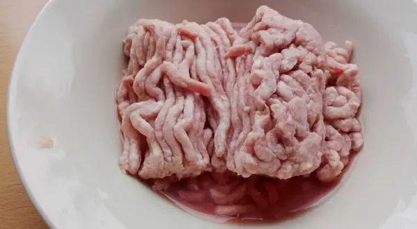 Mięso mielone w misce. Zwróć uwagę na podejrzany kolor i płyn, by rozpoznać objawy zepsutego mięsa mielonego.