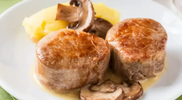 Dwa soczyste medaliony z polędwicy wieprzowej z pieczarkami i puree ziemniaczanym. Idealna temperatura dla polędwicy wieprzowej to 63°C.