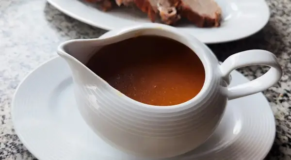 Aromaticzny sos do pieczeni w sosjerce, obok talerz z pokrojonym mięsem. Idealny dodatek, by dowiedzieć się, jak zrobić sos do pieczeni.