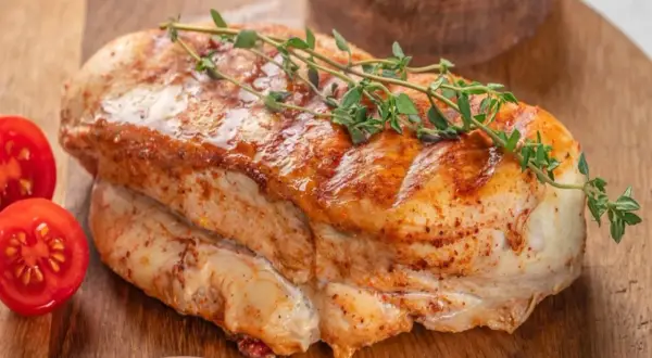 Soczysty filet z indyka duszony, z gałązką tymianku i pomidorkami koktajlowymi na desce.