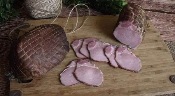 Jak zrobić soczysty schab wędzony? Na desce leżą dwa wędzone kawałki schabu, jeden w całości, drugi pokrojony w plastry.
