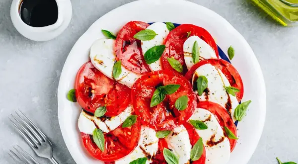Sałatka caprese z pomidorami i mozzarellą. Woda w sałatce może pojawić się z powodu dojrzałości pomidorów lub nadmiaru sosu.