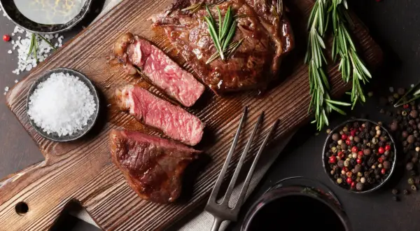 Soczysty rump steak, idealnie wysmażony, z gałązkami rozmarynu, solą i pieprzem. Obok kieliszek czerwonego wina.