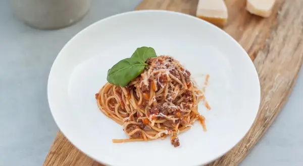 Porcja spaghetti z sosem bolognese, posypana parmezanem i udekorowana bazylią. Idealne danie, gdy chcesz wiedzieć, jak zawekować sos bolognese na później.