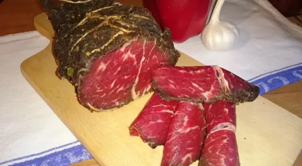 Pokrojona wołowina w paski na desce, obok papryka i czosnek. Idealna do dalszej obróbki, jak kroić wołowinę w paski.