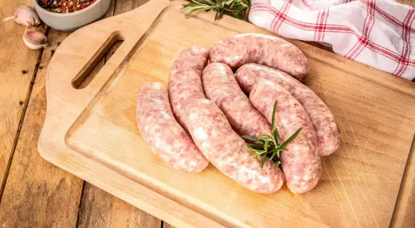 Surowa biała kiełbasa na desce, gotowa do przyrządzenia. Dowiedz się, jak długo gotować białą kiełbasę, by była idealna.