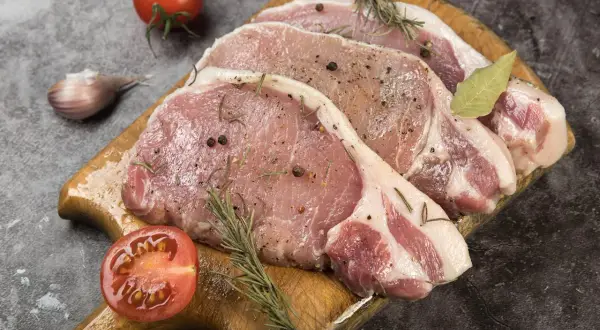 Surowe kotlety schabowe z przyprawami, gałązkami rozmarynu, czosnkiem i pomidorem. Zastanawiasz się, jak długo wędzić schab bez parzenia?