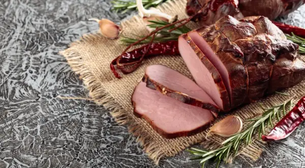 Wędzony schab, pokrojony w plastry, z czosnkiem, rozmarynem i papryczkami chili. Idealny przykład, jak zamarynować schab do wędzenia.