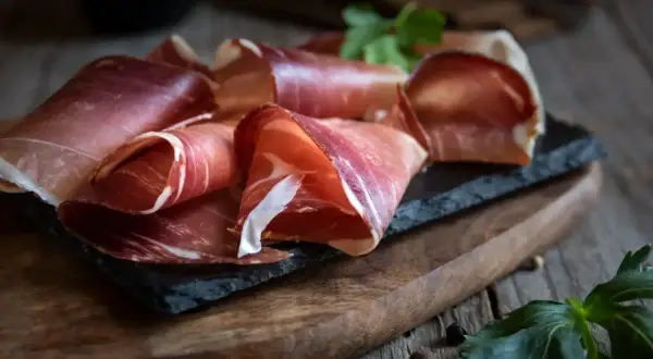 Plastry dojrzewającej szynki na desce. Idealne do nauki jak peklować szynkę na mokro proporcje soli i wody na kilogram.