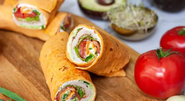 Pyszna tortilla z szynką, świeżymi warzywami i kremowym serkiem, ułożona na desce z dodatkami.