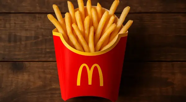 Czerwone pudełko z frytkami McDonald's na drewnianym tle.