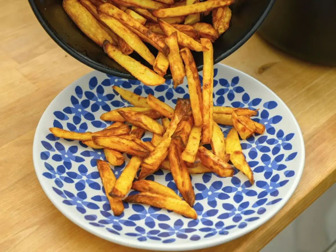 Złociste frytki, od cienkich shoestring po grubsze steak fries, wysypują się z patelni na talerz.