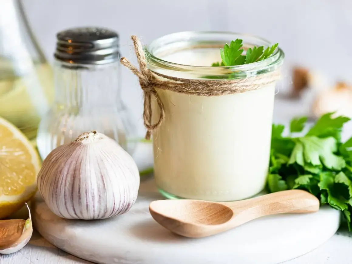 Sos aioli w słoiku, czosnek, cytryna i zioła. Różnica między sosem aioli a klasycznym majonezem czosnkowym jest subtelna, ale wyczuwalna.