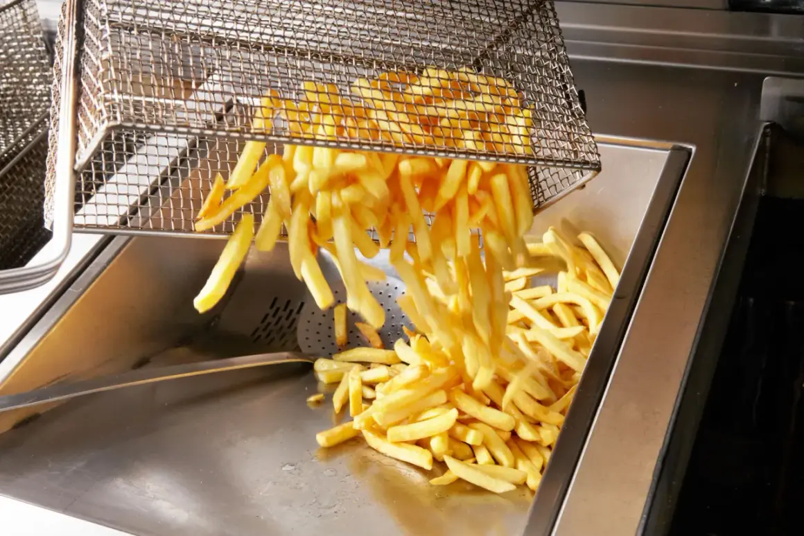 Frytki wysypywane z kosza do frytownicy. Nadmiar cukru w ziemniaku może powodować ciemnienie frytek podczas smażenia.