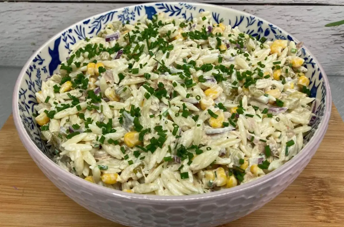 Pyszna sałatka z tuńczykiem i makaronem orzo, z kukurydzą i szczypiorkiem, w ozdobnej misce.