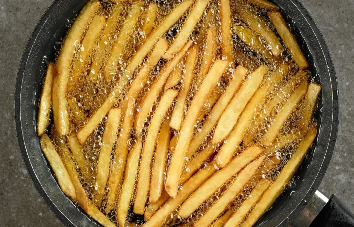 Smażone frytki w gorącym oleju. Aby uniknąć nasiąkania frytek tłuszczem, kluczowe jest utrzymanie wysokiej temperatury oleju.