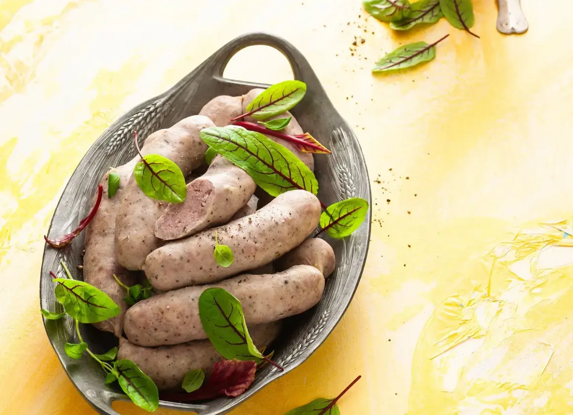 Domowa biała kiełbasa bez maszynki, podana w metalowej misie z liśćmi szczawiu.