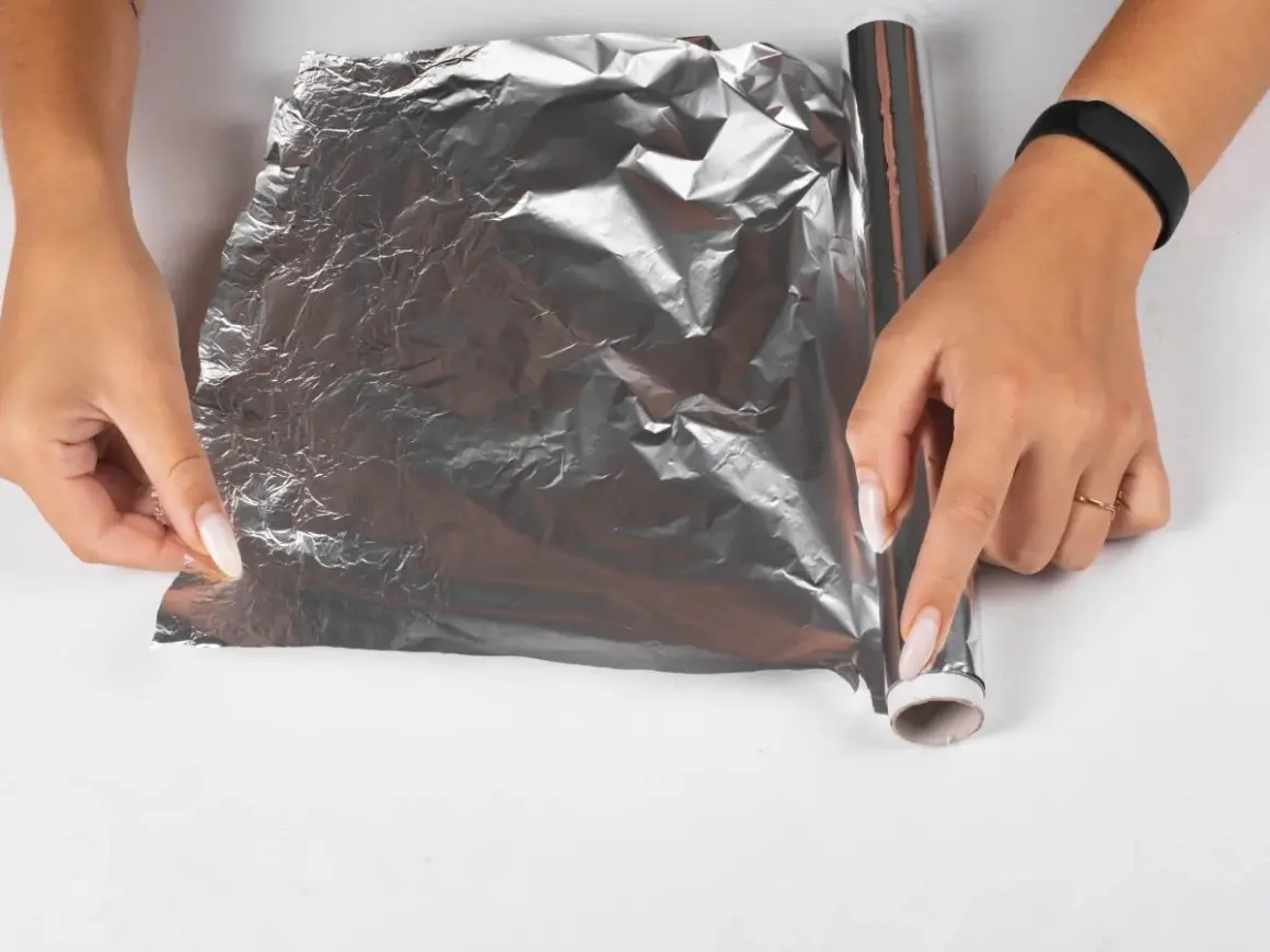 Dłonie rozwijają folię aluminiową, by zapobiec powstawaniu kożucha na sosie. Jak go zabezpieczyć folią?