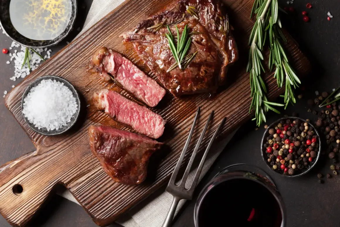 Soczysty rump steak, idealnie wysmażony, z gałązkami rozmarynu, solą i pieprzem. Obok kieliszek czerwonego wina.
