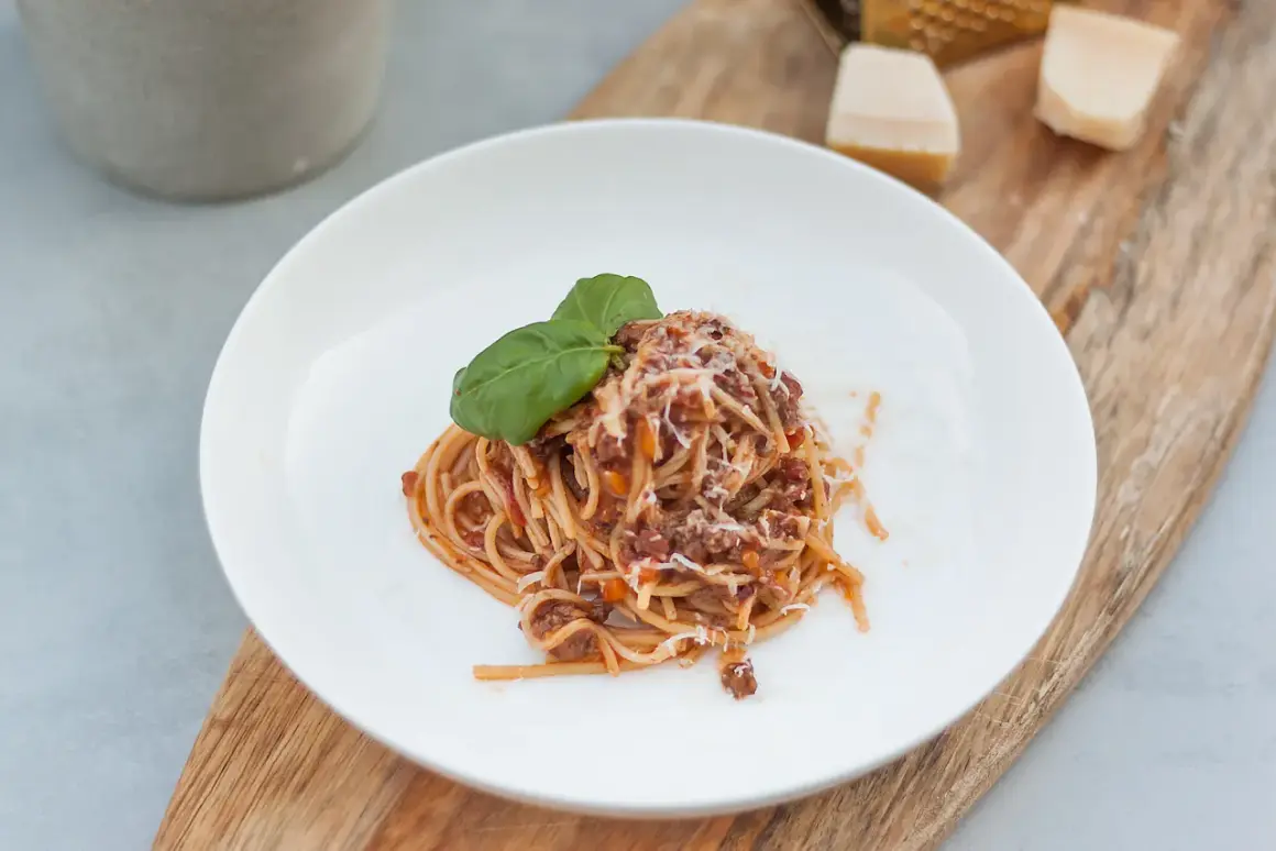 Porcja spaghetti z sosem bolognese, posypana parmezanem i udekorowana bazylią. Idealne danie, gdy chcesz wiedzieć, jak zawekować sos bolognese na później.