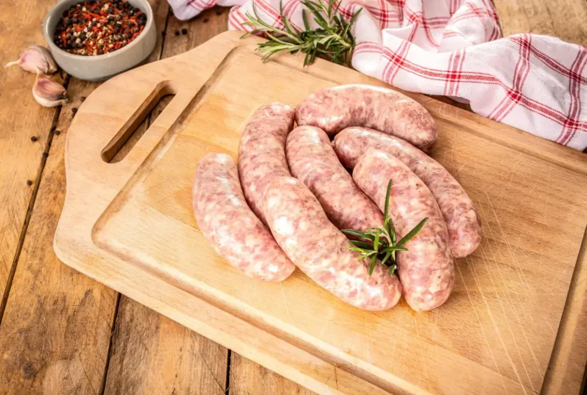 Surowa biała kiełbasa na desce, gotowa do przyrządzenia. Dowiedz się, jak długo gotować białą kiełbasę, by była idealna.