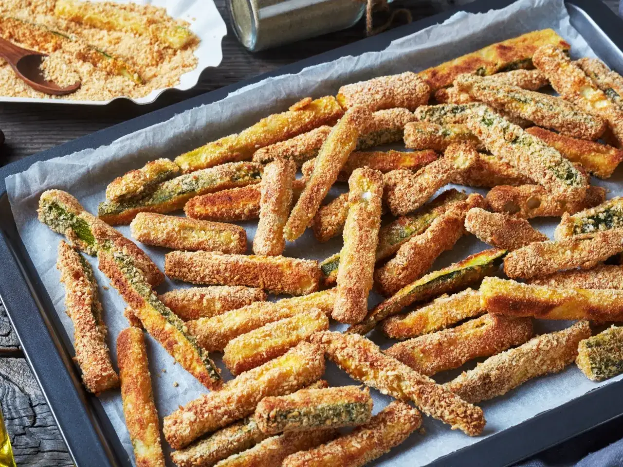 Tak, frytki z cukinii można zrobić w panierce panko. Na blasze wyłożonej papierem do pieczenia leżą złociste, chrupiące słupki cukinii w panko.