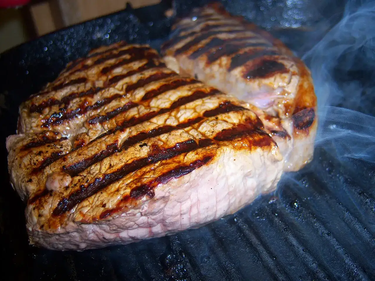 Dwa soczyste steki rump steak grillują się na patelni, wydzielając apetyczny dym.