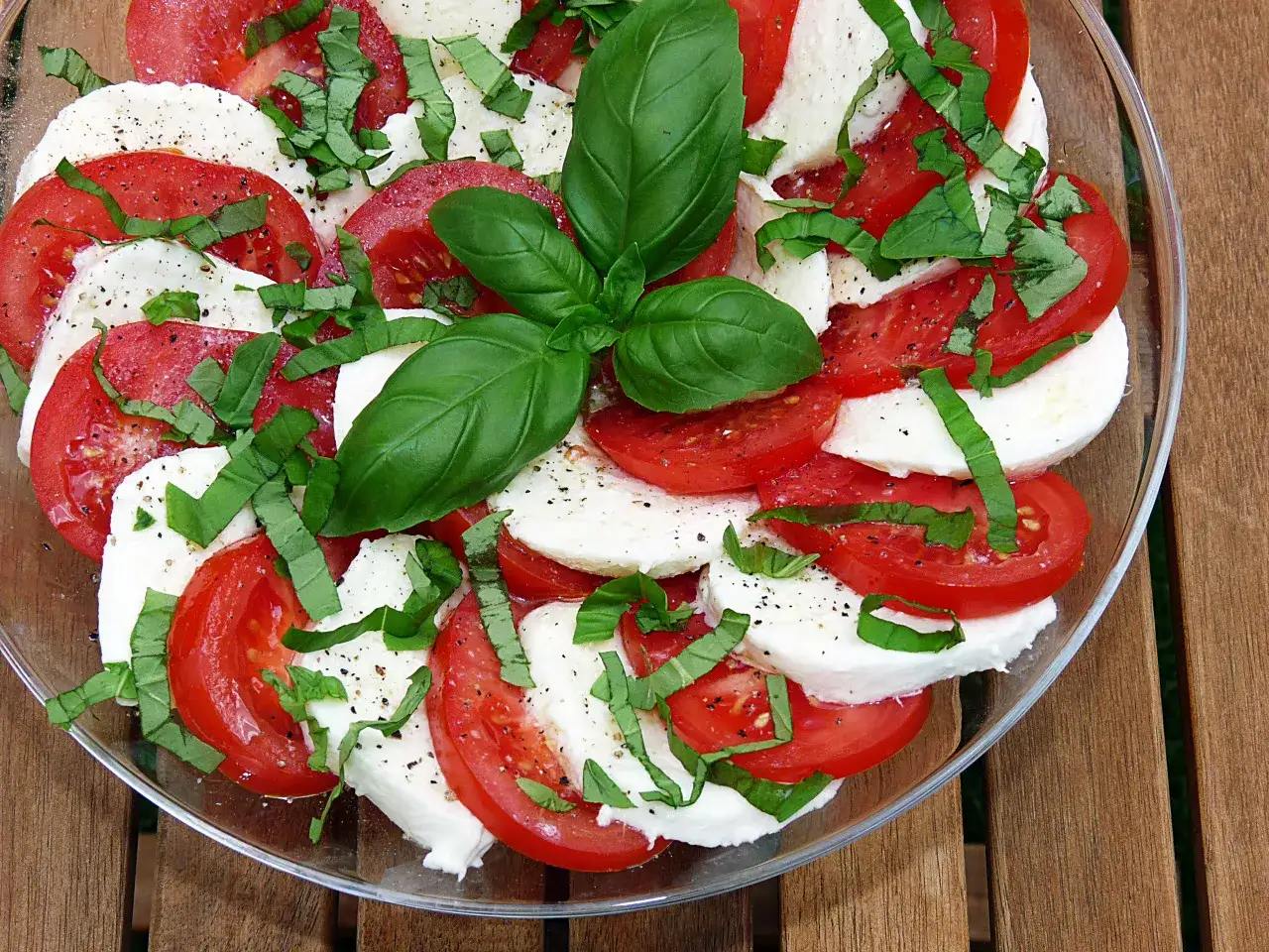 Sałatka Caprese z pomidorów i mozzarelli, posypana bazylią. Woda na dnie talerza może świadczyć o świeżości składników.