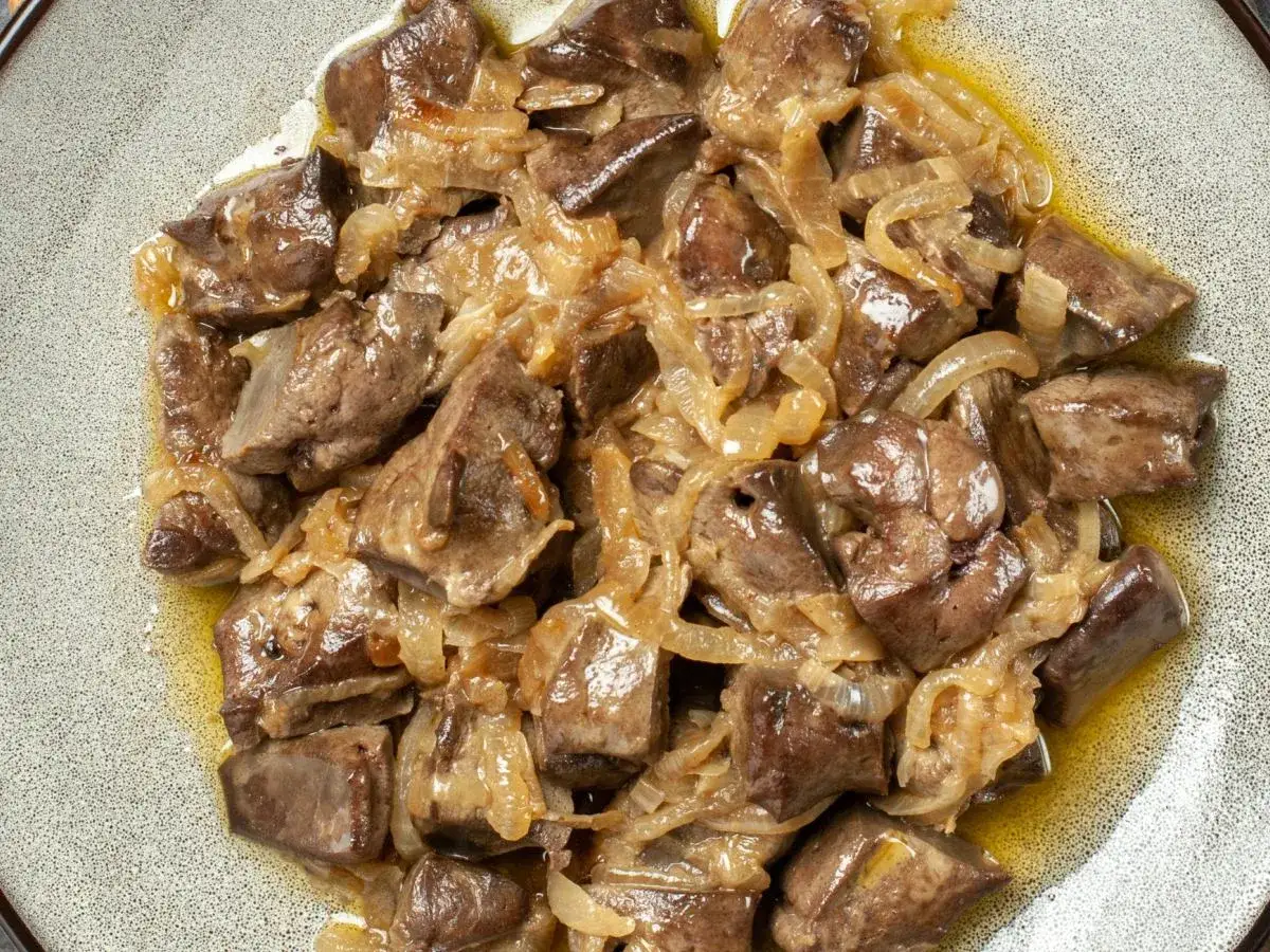 Jak przygotować wątróbkę drobiową do smażenia? Pokrojona wątróbka duszona z cebulką na talerzu.