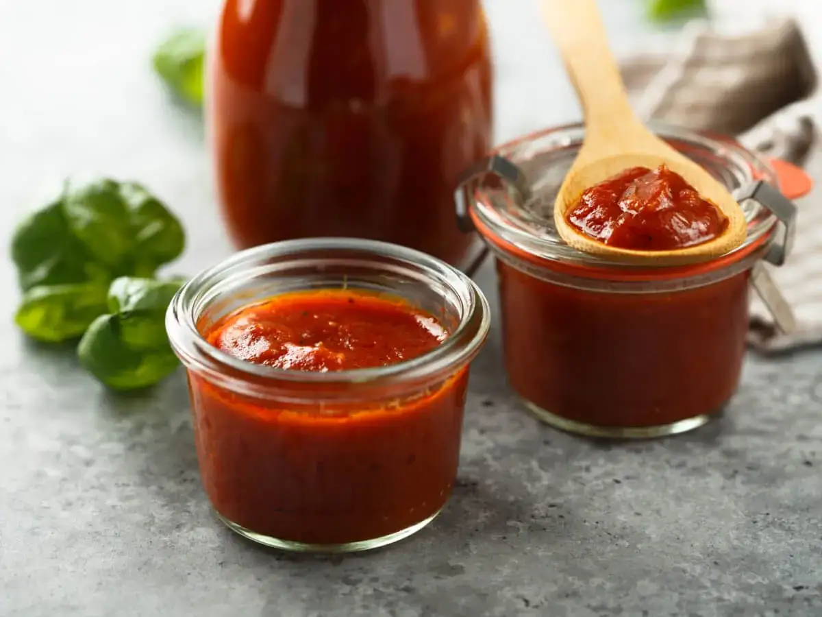 Domowy ketchup do frytek o niskiej zawartości cukru w słoiczkach, z łyżką i listkami bazylii.