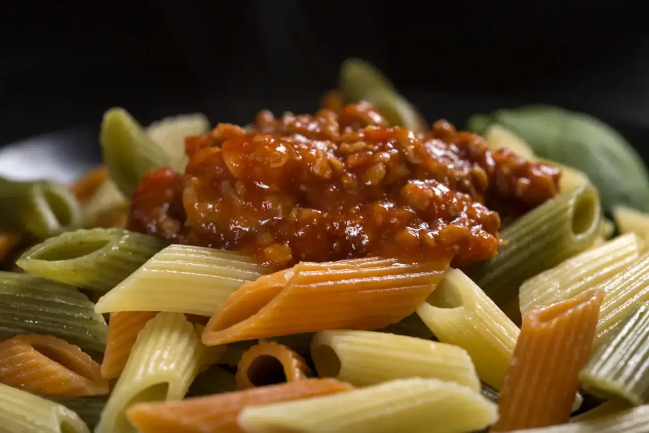 Kolorowy makaron penne z sosem bolońskim. Zasady przywierania sosu do makaronu spaghetti i penne są kluczowe dla smaku.