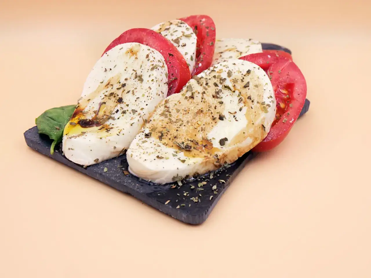 Sałatka caprese z pomidorami i mozzarellą, przyprawiona ziołami. Woda na talerzu może wynikać z soczystości pomidorów.