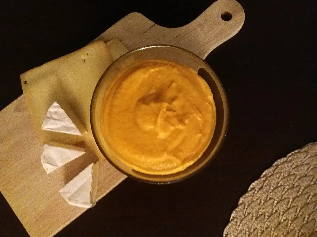 Pomarańczowy sos serowy w szklanej miseczce, obok kawałki sera na desce. Uważaj, by nie przegrzać sosu serowego, bo zrobi się gumowaty.
