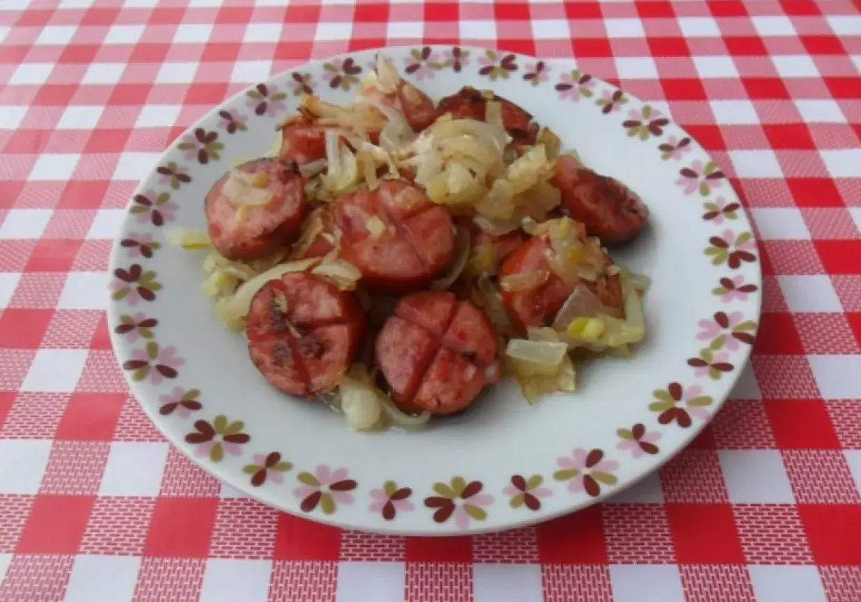 Pokrojona kiełbasa smażona z cebulą na patelni. Idealny sposób, by dowiedzieć się, ile smażyć kiełbasę na patelni, by była pyszna.