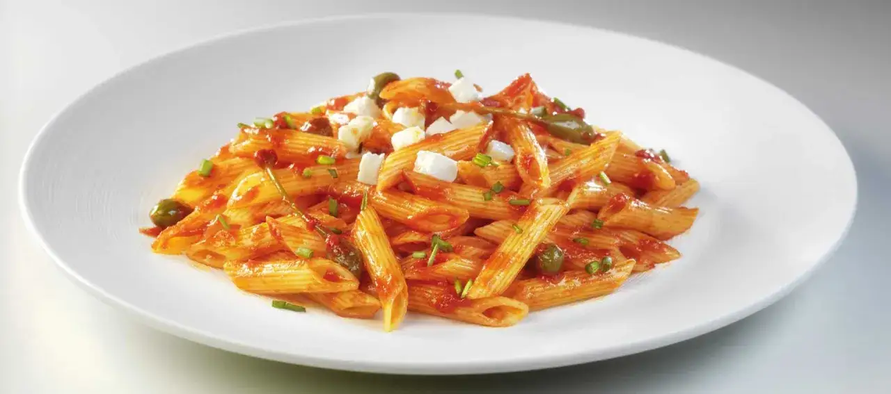 Penne w sosie pomidorowym z fetą i oliwkami. Sos jest gęstszy niż klasyczna passata, co sugeruje różnicę między sosem marinara a klasyczną passatą pomidorową.