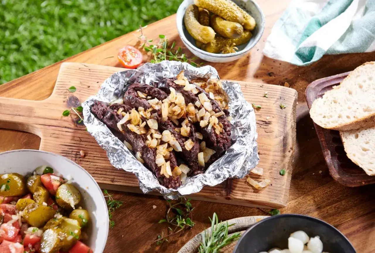 Kaszanka zapiekana z cebulką na drewnianej desce, podana z ogórkami kiszonymi i pieczywem. Idealny sposób, jak przyrządzić kaszankę na grillu.