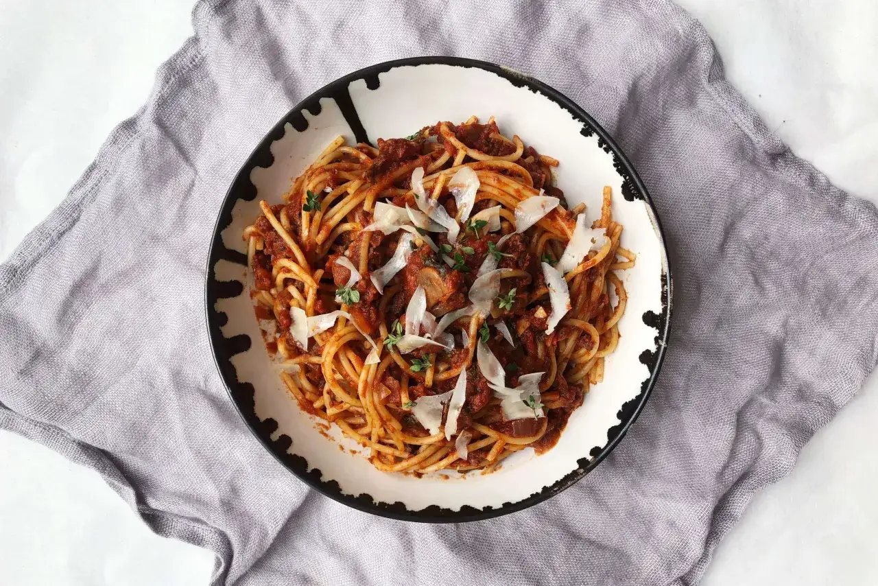 Spaghetti z bogatym sosem bolońskim, posypane parmezanem i ziołami. Długie gotowanie sosu to klucz do głębi smaku.