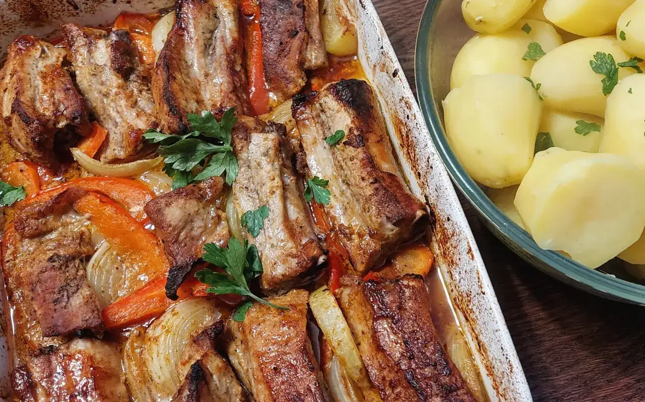 Pyszne, pieczone żeberka z warzywami w naczyniu żaroodpornym, obok miska z gotowanymi ziemniakami. Idealne na obiad!