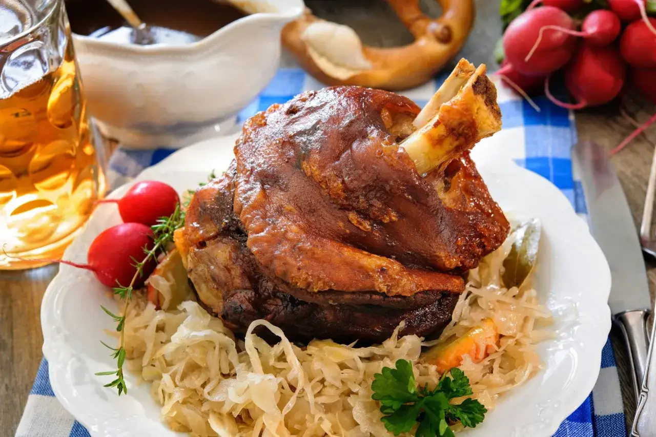 Soczysta golonka pieczona w piekarniku, podana z kapustą kiszoną, rzodkiewkami i kuflem piwa.