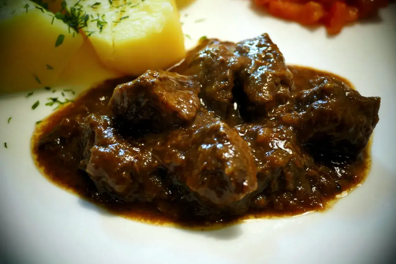 Soczyste kawałki mięsa w sosie, obok ziemniaki posypane koperkiem. Idealne danie, które pokazuje, czy marynować mięso na gulasz.