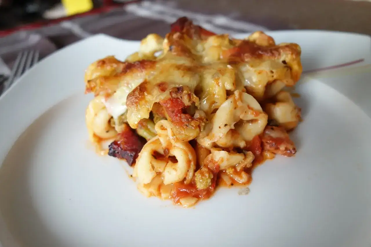 Zapiekane tortellini w sosie pomidorowym, z ciągnącym się serem i kawałkami boczku. Pyszne danie na talerzu.
