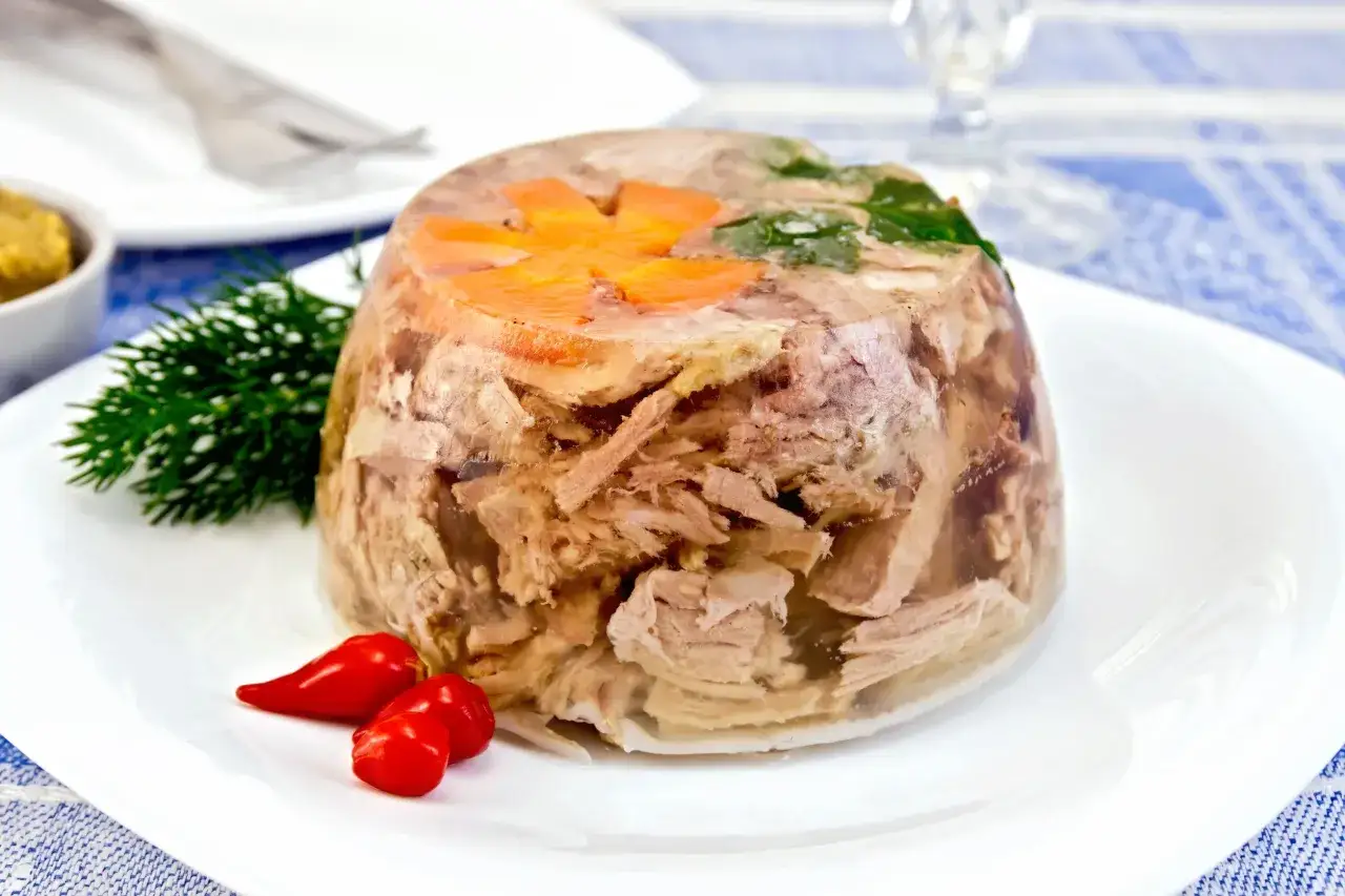 Pyszna galareta wieprzowa z marchewką i koperkiem, ozdobiona papryczkami chili. Idealna do przechowywania w lodówce.