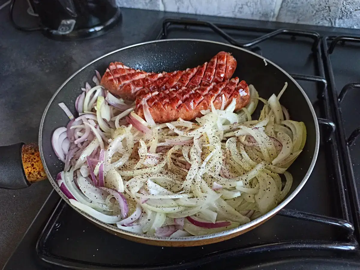 Kiełbasa skwierczy na patelni wśród cebuli. Dylemat: co smażyć pierwsze, kiełbasę czy cebulę?