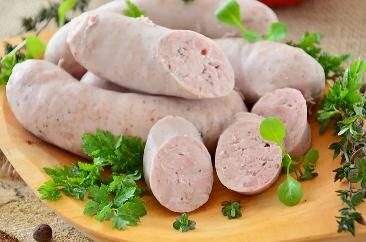 Domowa biała kiełbasa bez maszynki, pyszna i soczysta, na drewnianej desce z ziołami.