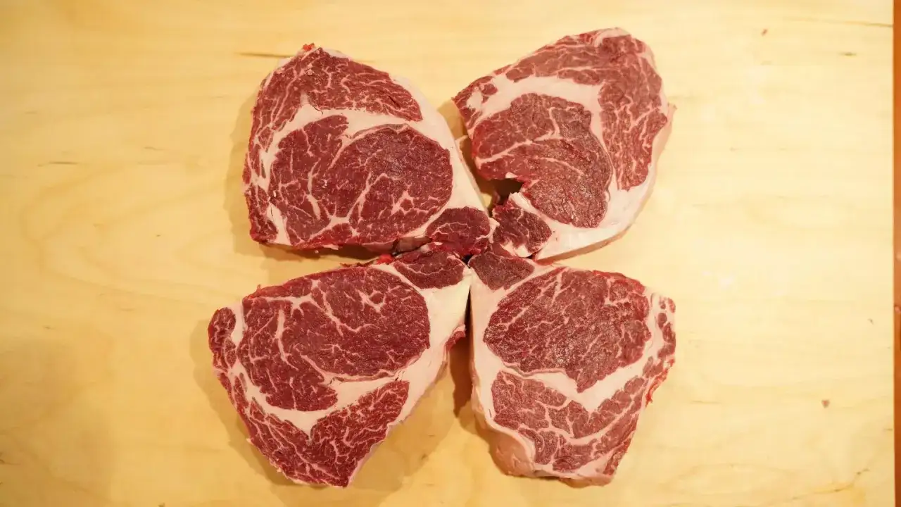 Cztery soczyste steki ribeye z widocznym marmurkowaniem. Jak rozpoznać wołowinę z chowu pastwiskowego od przemysłowej? Zwróć uwagę na tłuszcz.