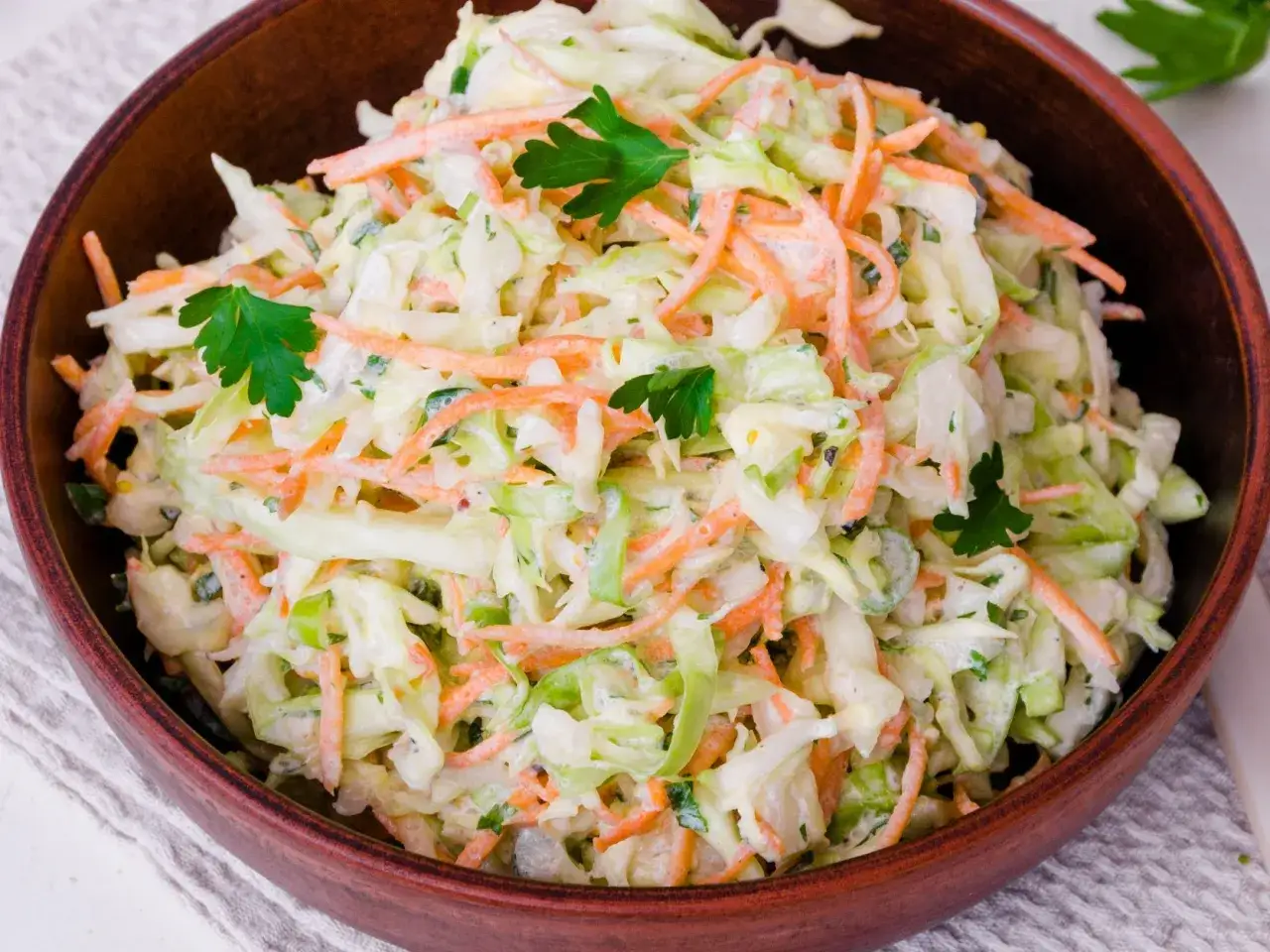 Kremowa sałatka coleslaw z tartą marchewką i posiekaną natką pietruszki, która odróżnia ją od klasycznej surówki z kapusty.